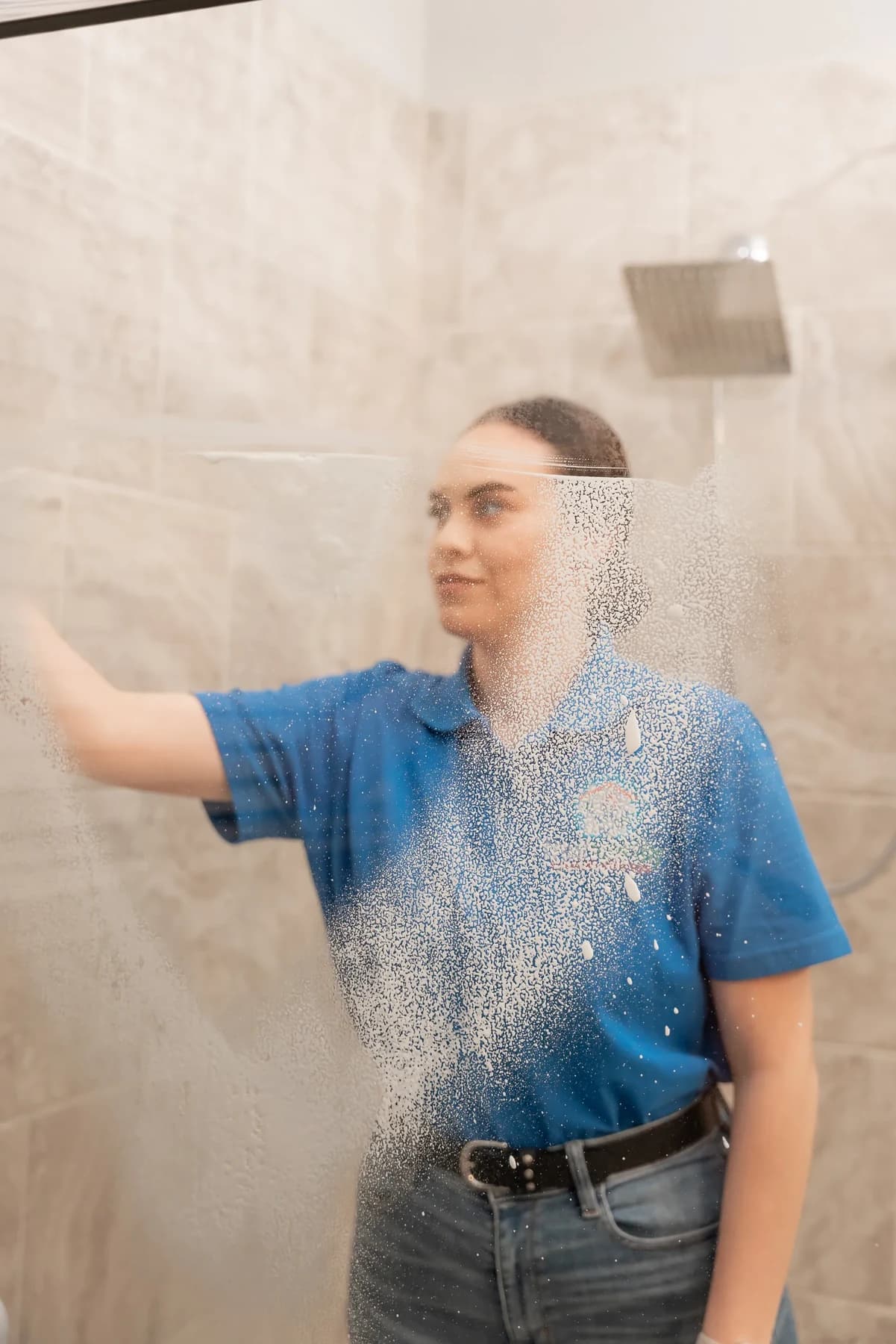 Cleaner cleaning a tiled shower and glass door