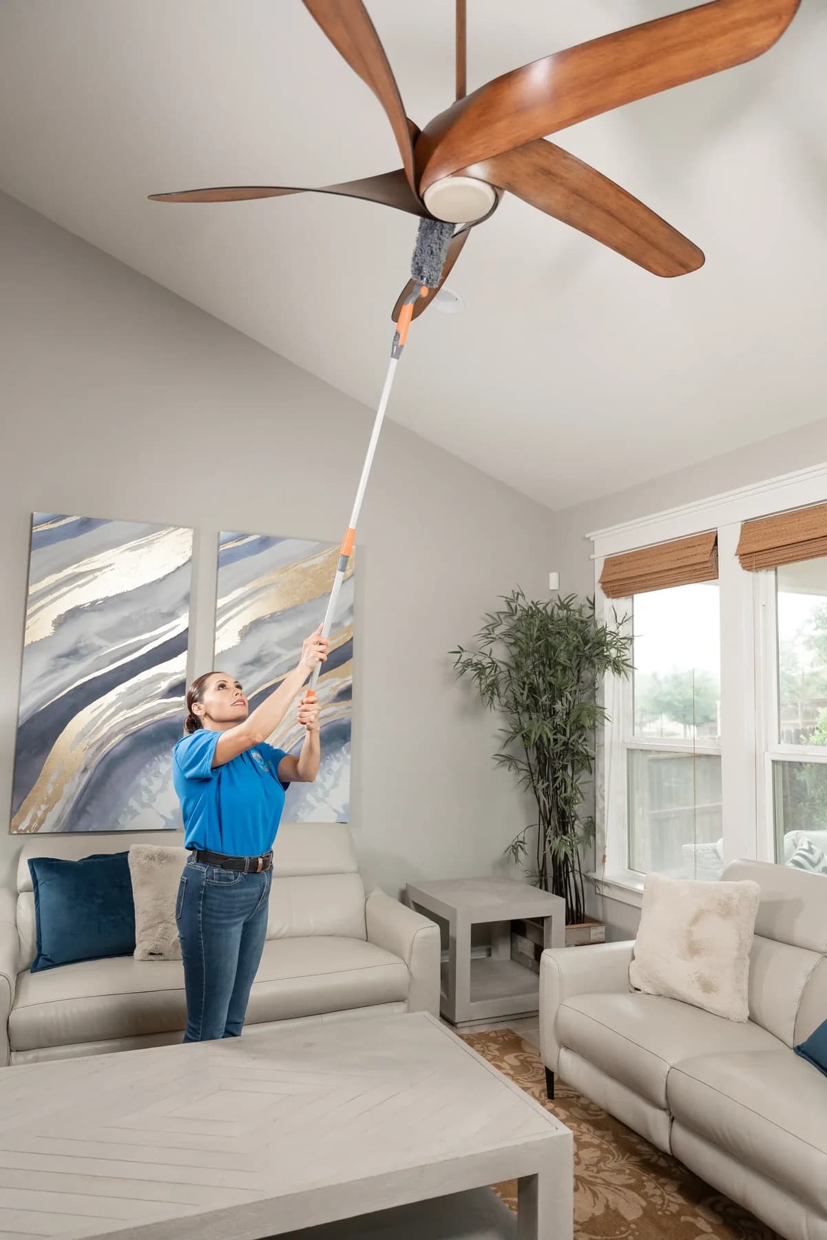 Cleaner dusting ceiling fan blades during a house cleaning