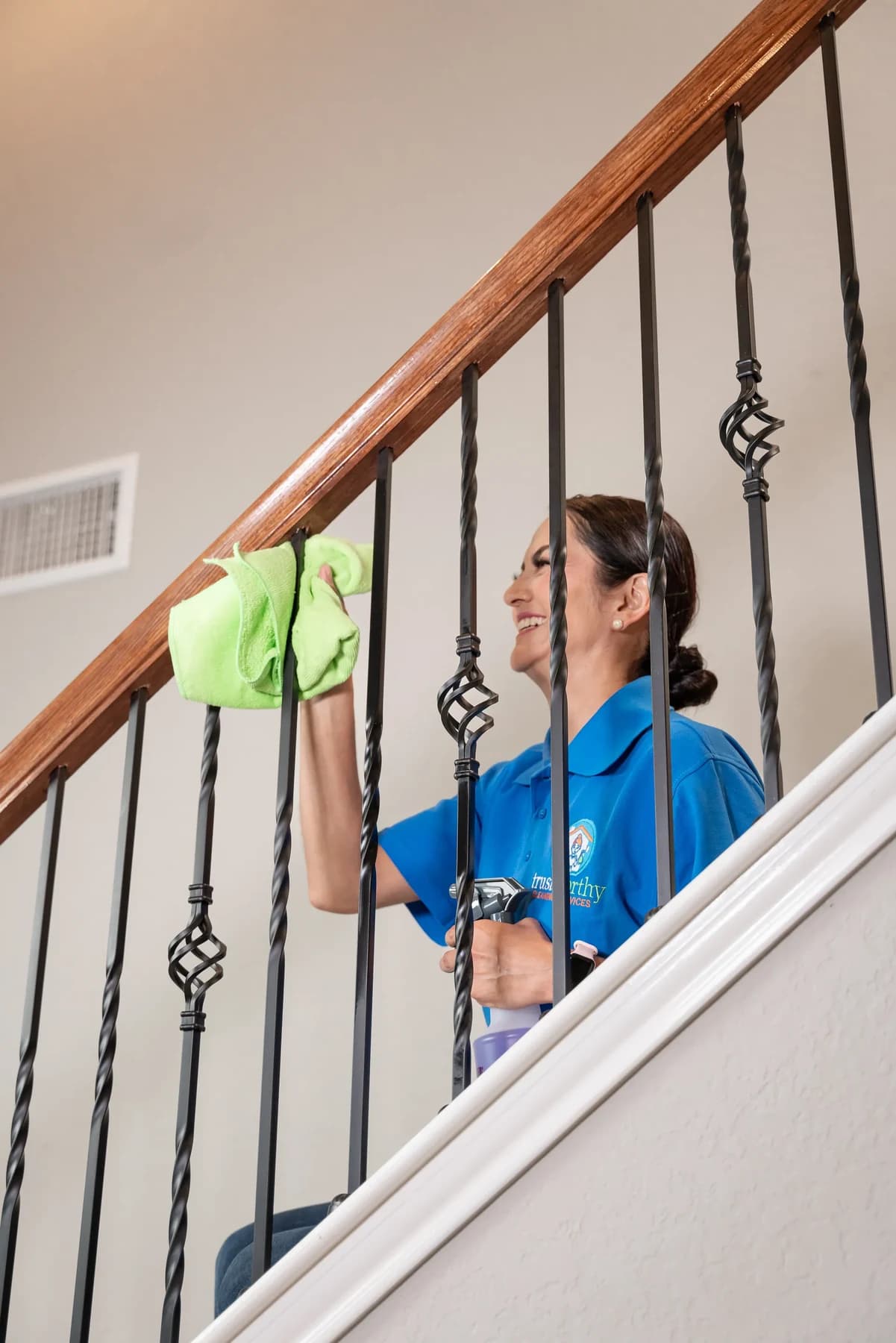 Cleaner wiping a stair handrail in a two-story Austin home