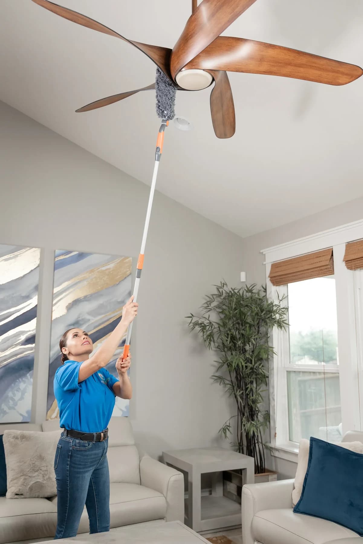 Cleaner dusting ceiling fan blades during a house cleaning
