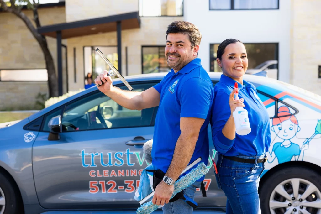 Two Trustworthy Cleaning Services team members holding squeegees and supplies in front of the branded company van in Austin, Texas