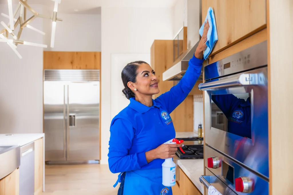 Trustworthy Cleaning Services team member wiping a stainless steel oven front in a commercial break room kitchen in Austin, Texas